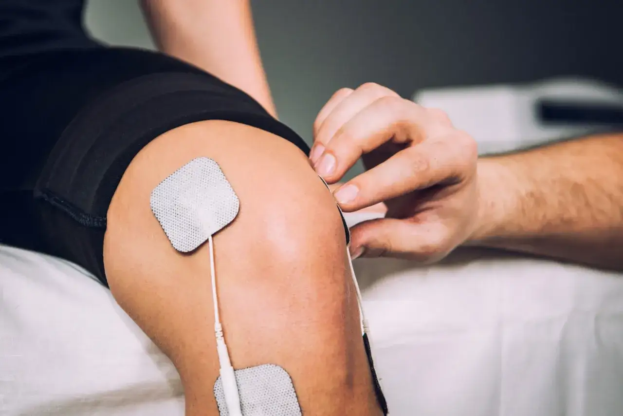 Dłoń terapeuty umieszcza elektrody na kolanie pacjenta, przygotowując do sesji ems trening.