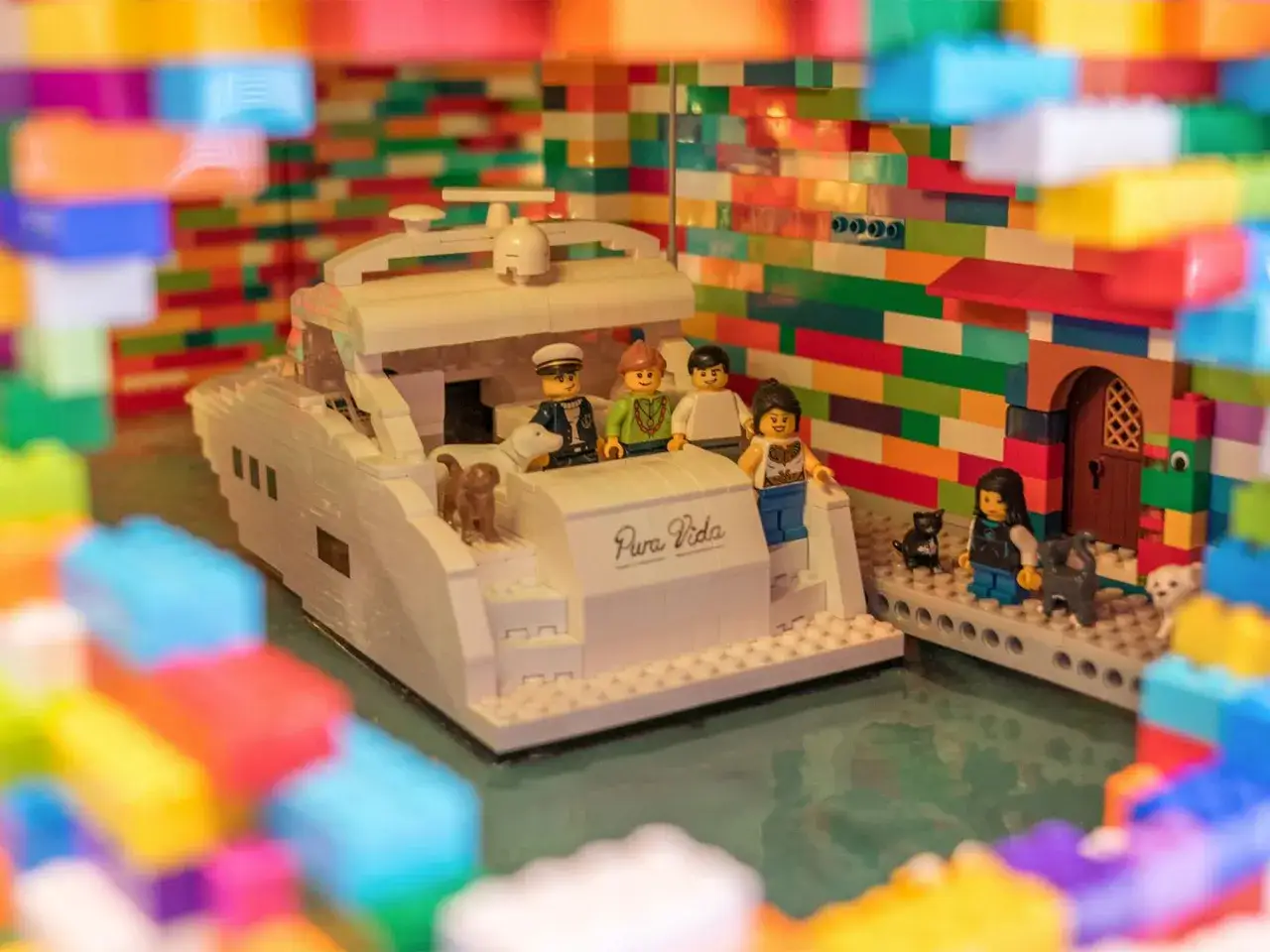 Bunte LEGO MOCs: Eine Yacht mit Figuren und Tieren vor einem Haus mit bunten W&auml;nden.