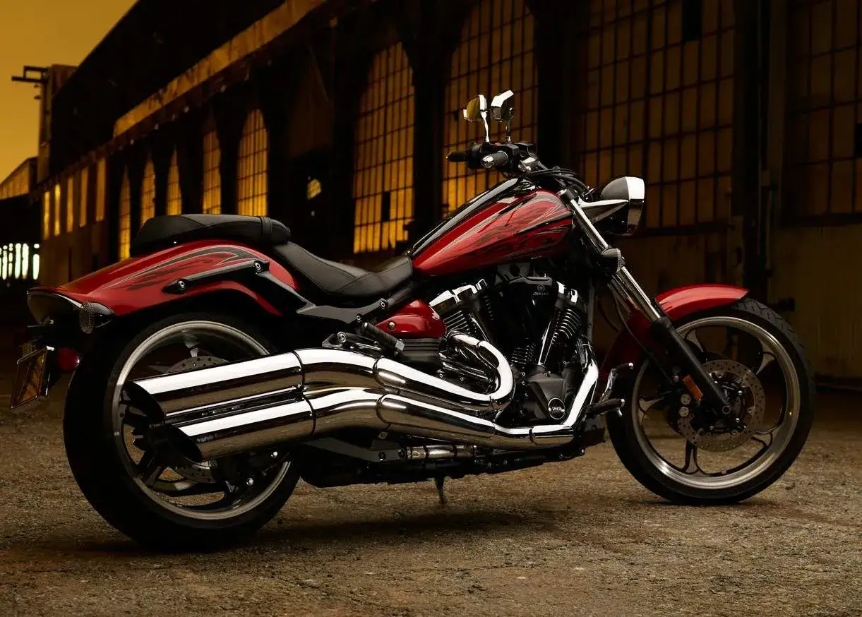 Czerwony motocykl Yamaha Raider 1900 z chromowanymi wydechami, stojący przed industrialnym budynkiem. Dane techniczne tego modelu są imponujące.