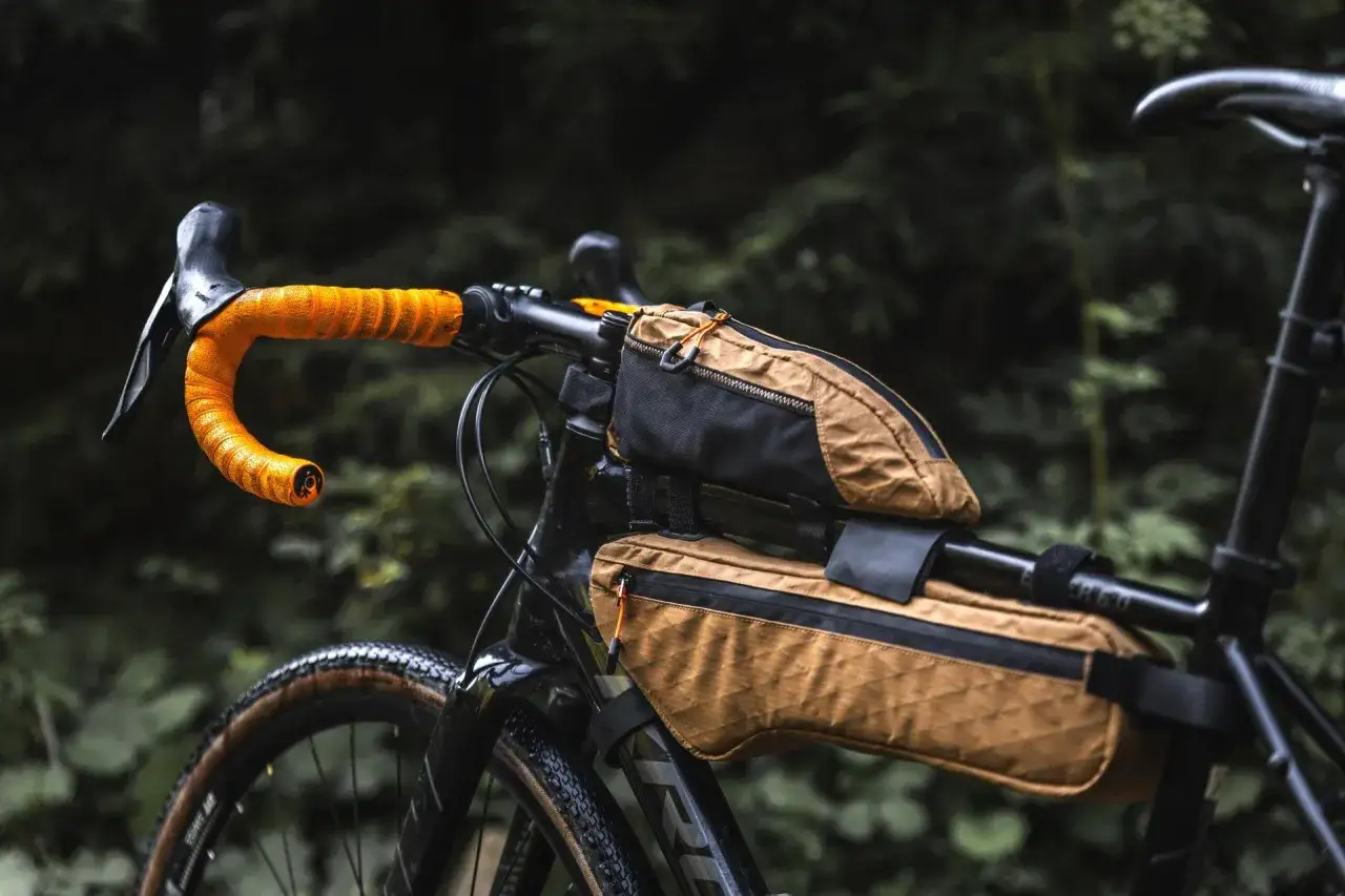 Rower gravelowy gotowy na przygodę, z pomarańczową owijką kierownicy i torbami do bike packingu.