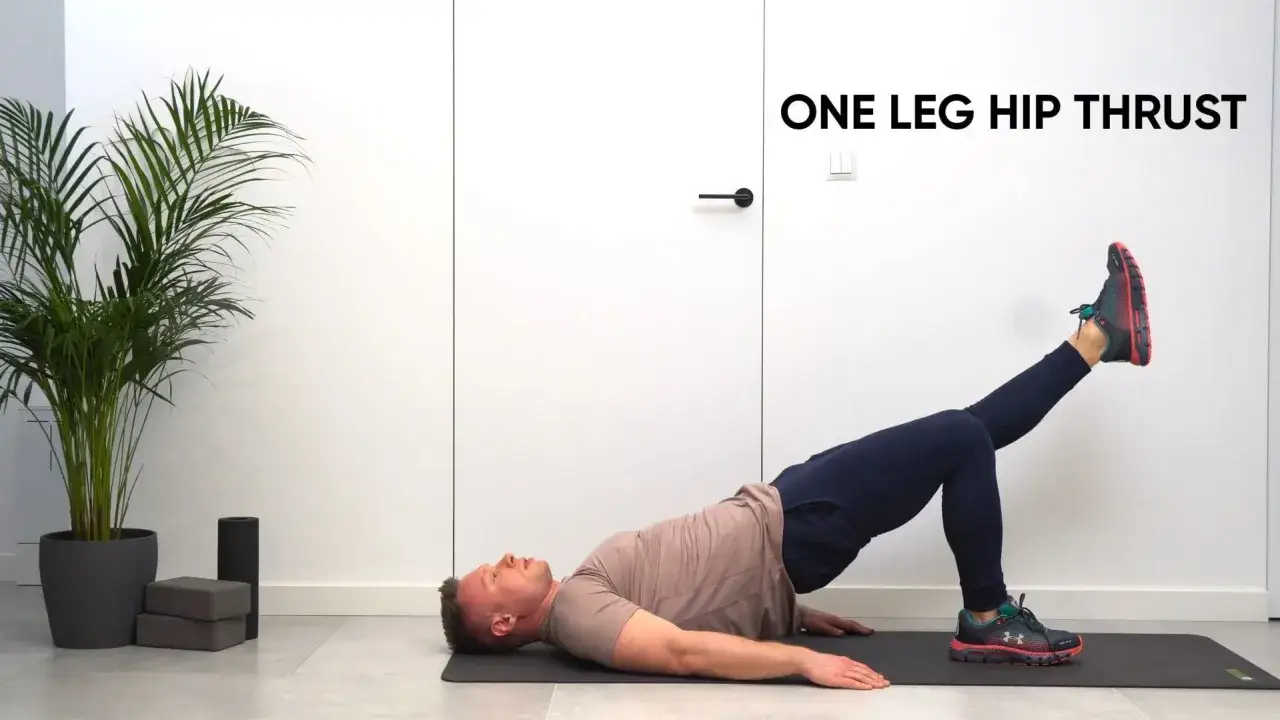 Mężczyzna wykonuje ćwiczenie hip thrust w domu, leżąc na macie z jedną nogą uniesioną.