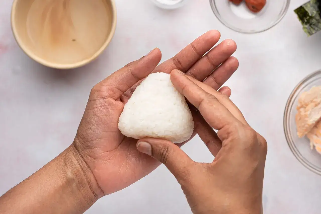 Hands shaping a perfectly formed onigiri. If yours fall apart, try pressing the rice more firmly.