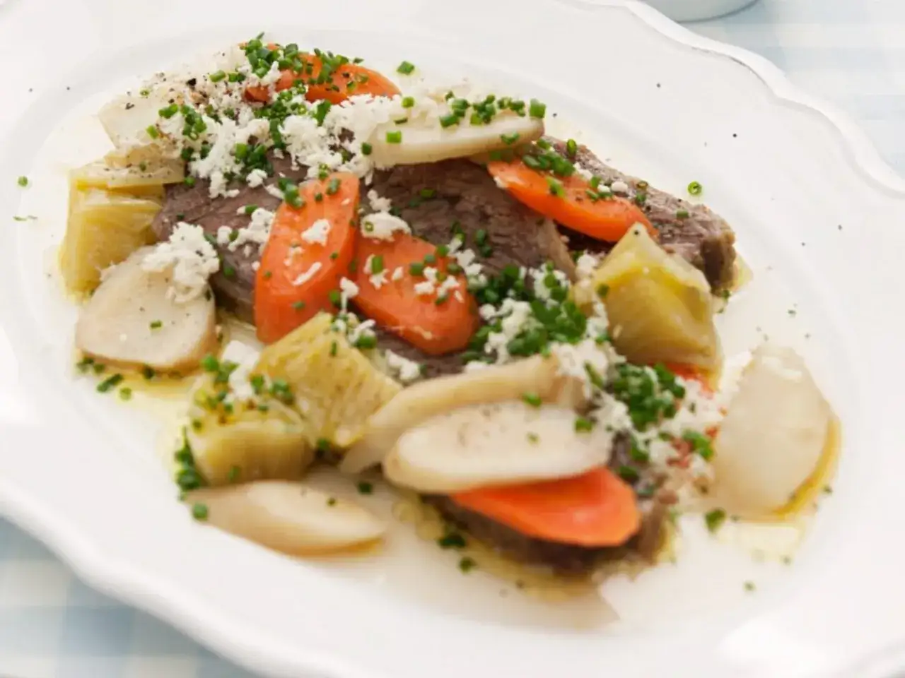 Ein köstliches Tafelspitz-Rezept mit zartem Rindfleisch, Karotten, Wurzelgemüse und frischen Kräutern, garniert mit geriebenem Käse.