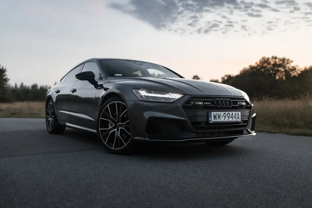 Elegancki Audi A7 2025 w ciemnym kolorze, zaparkowany na drodze o zachodzie słońca.