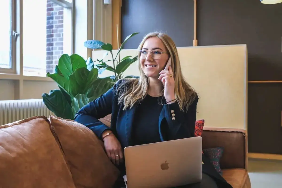 Kobieta w okularach rozmawia przez telefon, obok laptopa. Dyskutuje, ile czasu ma pracodawca na zgłoszenie pracownika do ZUS.
