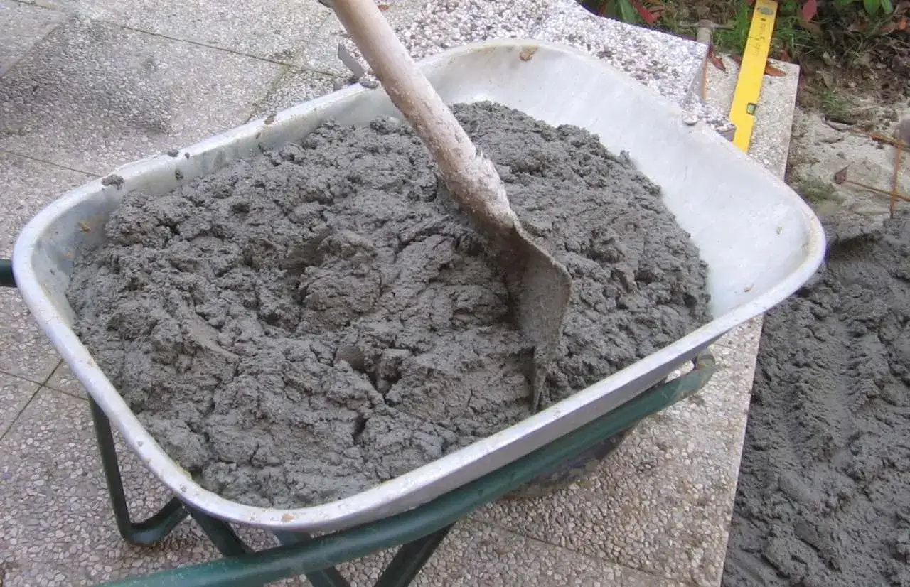 Carriola piena di malta composizione, con una pala che mescola il materiale grigio.