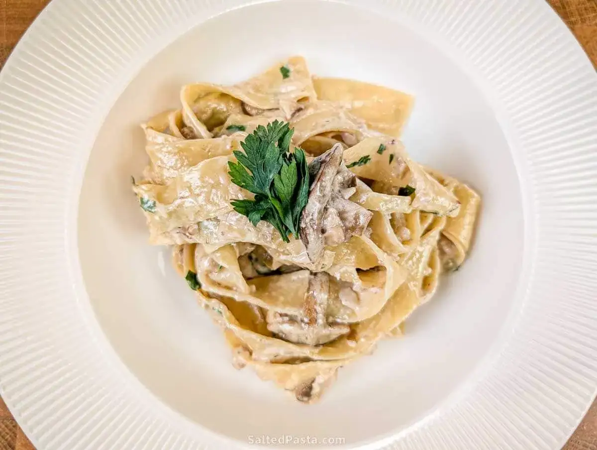 Pappardelle, czyli makaron długi płaski, w kremowym sosie grzybowym, udekorowany natką pietruszki.