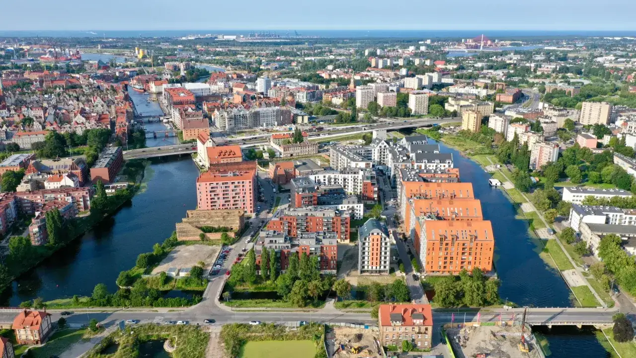 Widok na nowoczesne osiedle nad rzeką w Gdańsku, z charakterystyczną architekturą i zielenią. Chmielna w Gdańsku tętni życiem.
