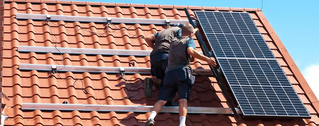 Tv&aring; m&auml;n installerar solpaneler p&aring; ett tegeltak. De arbetar med att f&auml;sta panelerna p&aring; monteringsskenorna.