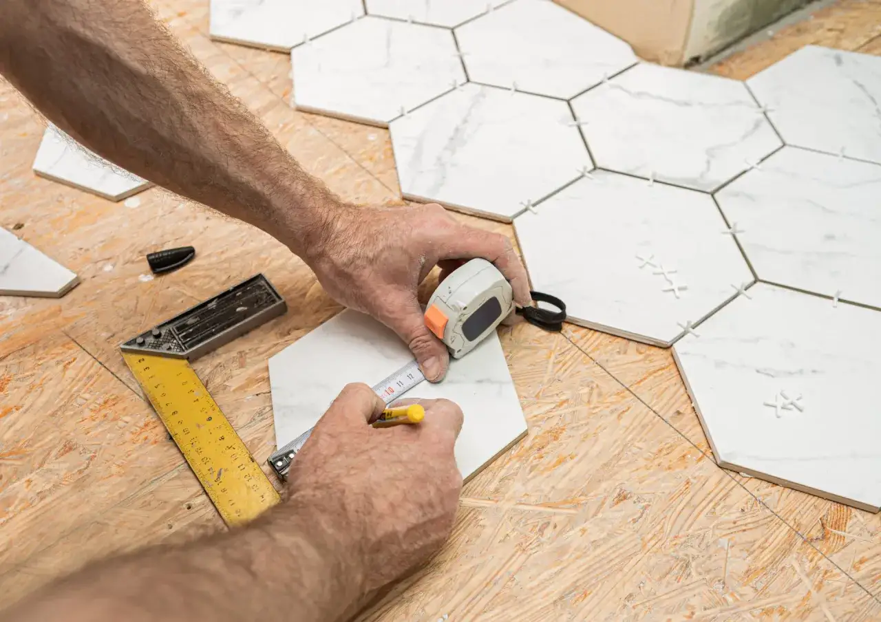 Pose de carreaux hexagonaux sur plancher OSB. Un carreleur mesure une pi&egrave;ce avant la pose.