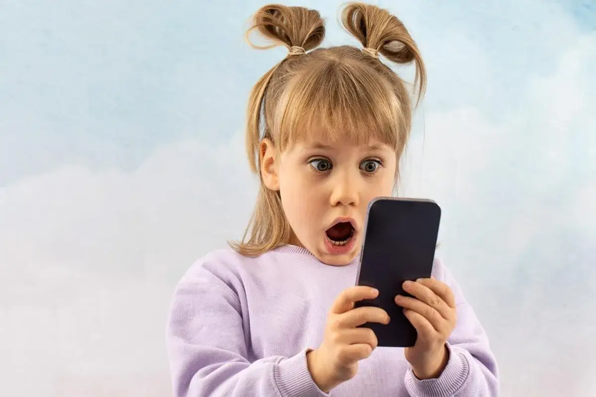 Zaskoczona dziewczynka z telefonem w ręku. Jak kontrolować telefon dziecka, by uniknąć takich min?