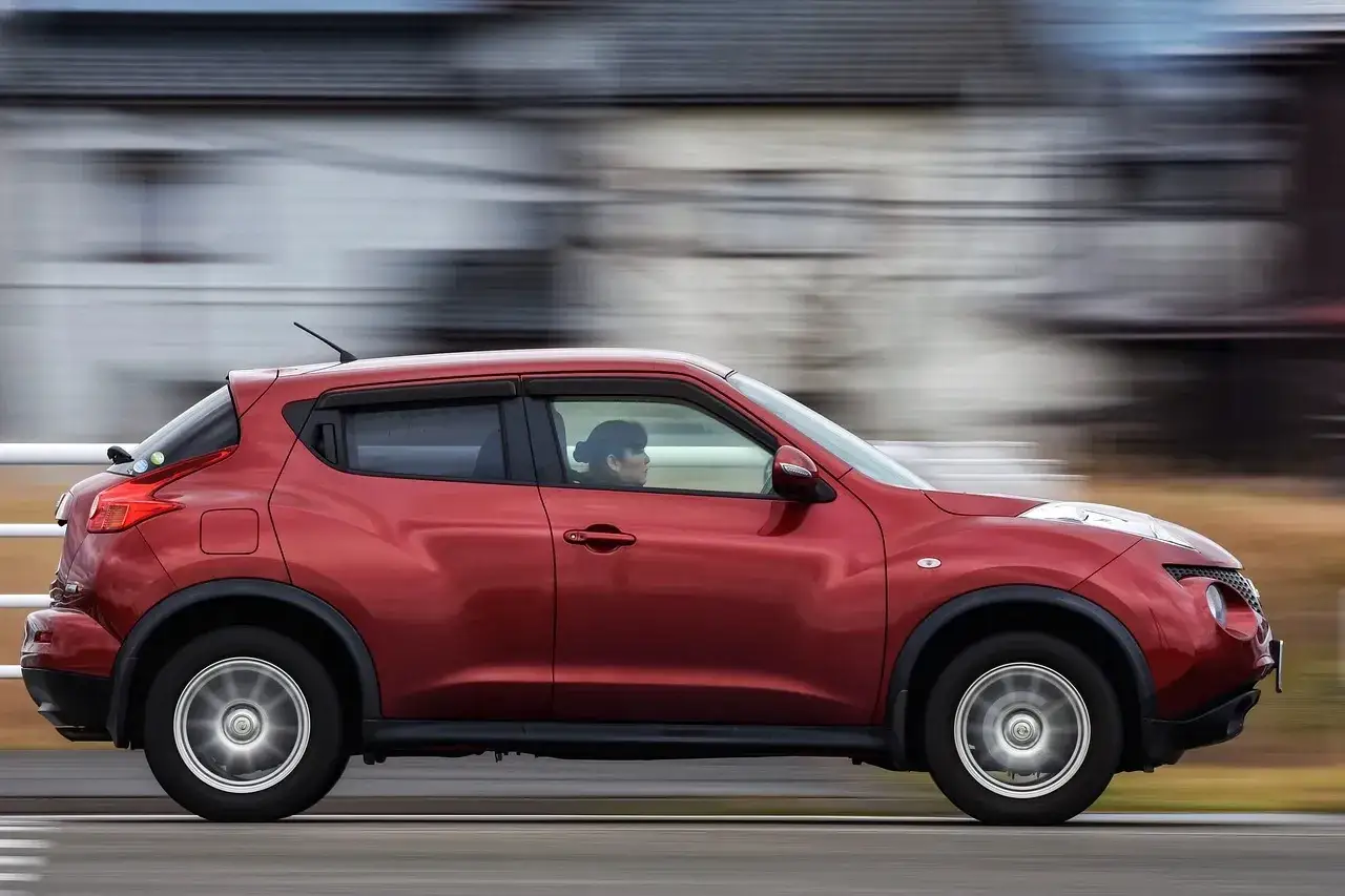 Czerwony Nissan Juke z kobietą za kierownicą pędzi po drodze. Jaka to marka? To Nissan!