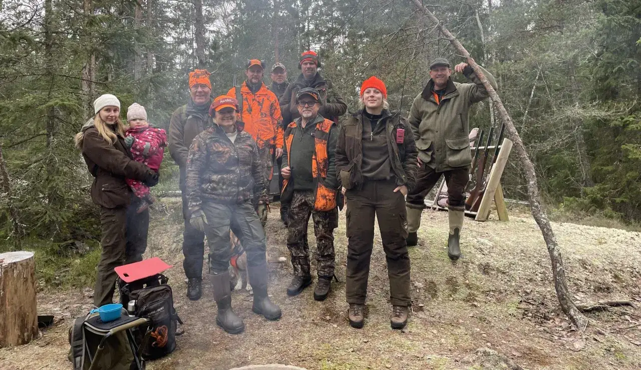 En grupp j&auml;gare i skogen, inklusive en kvinna med barn. De &auml;r kl&auml;dda i jaktkl&auml;der. Ingen indikation p&aring; jaktbrott eller straff.