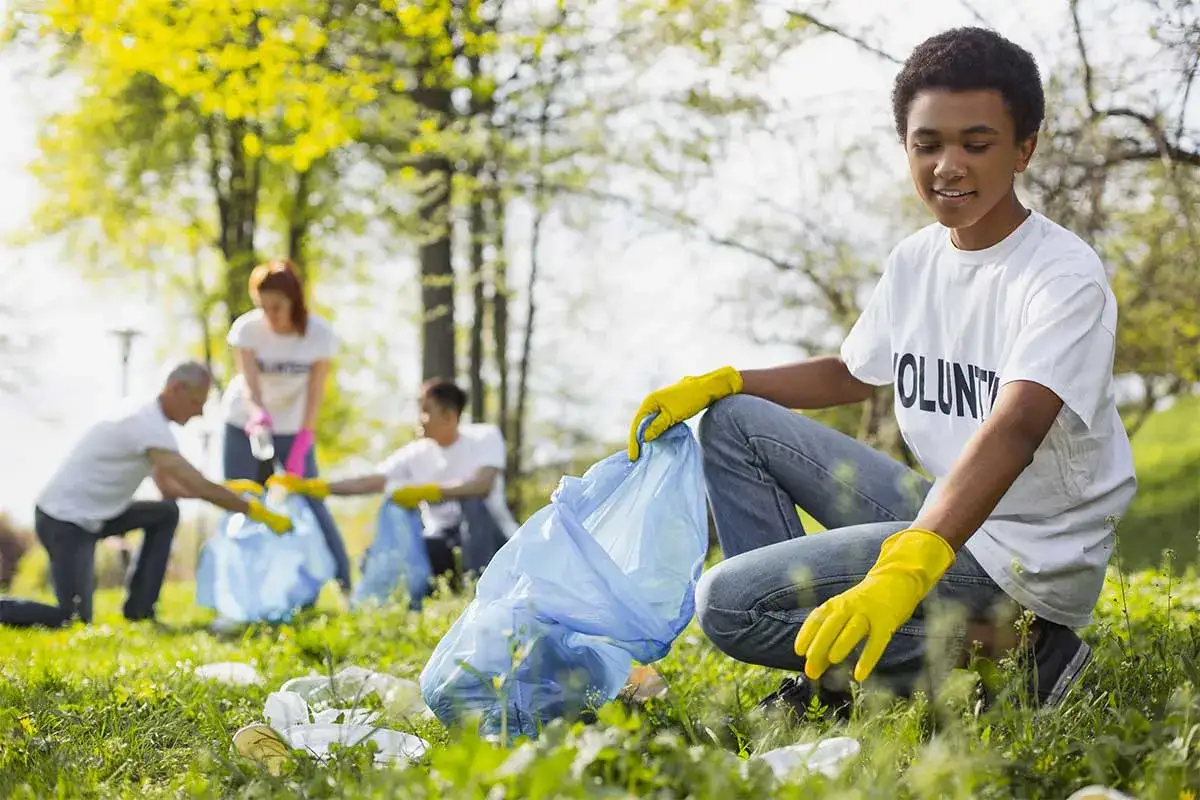 Young volunteer collecting trash in a park, part of a group engaged in community service ideas.