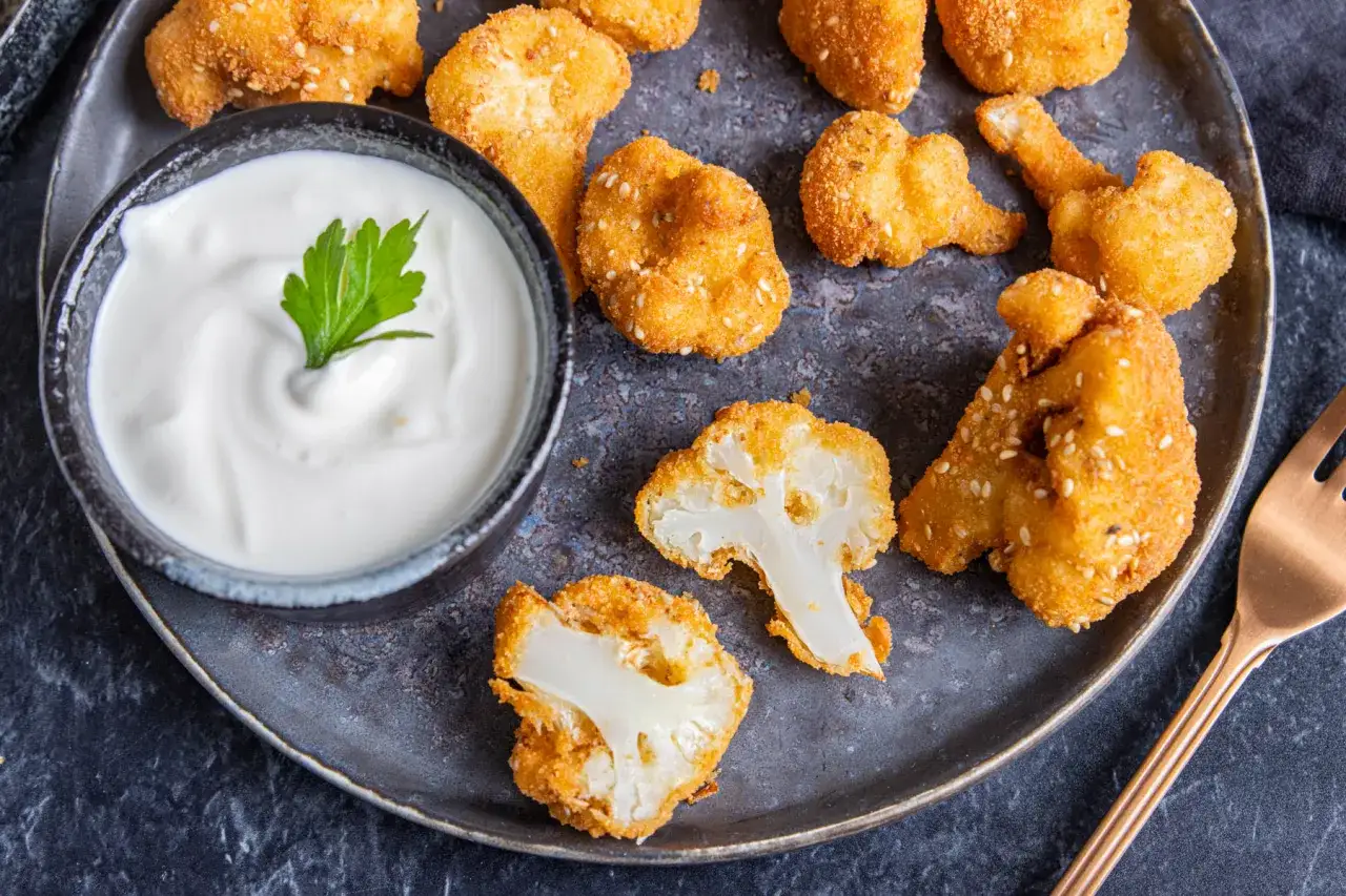 Knusprige blumenkohl nuggets ofen, goldbraun gebacken, mit einem cremigen Dip und Petersilie garniert.