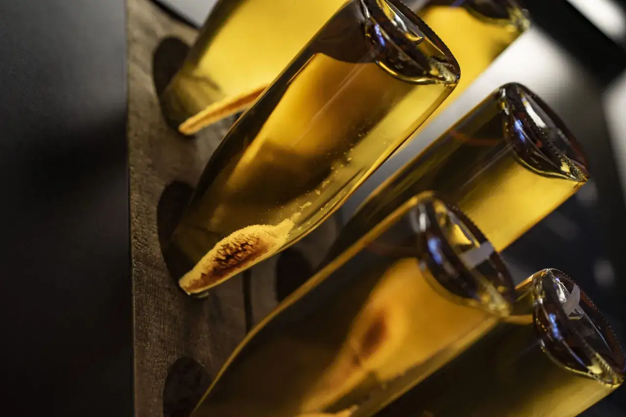Flaschen mit goldgelbem Champagner in einem Holzgestell, die auf die Champagner Herstellung und Reifung hinweisen.