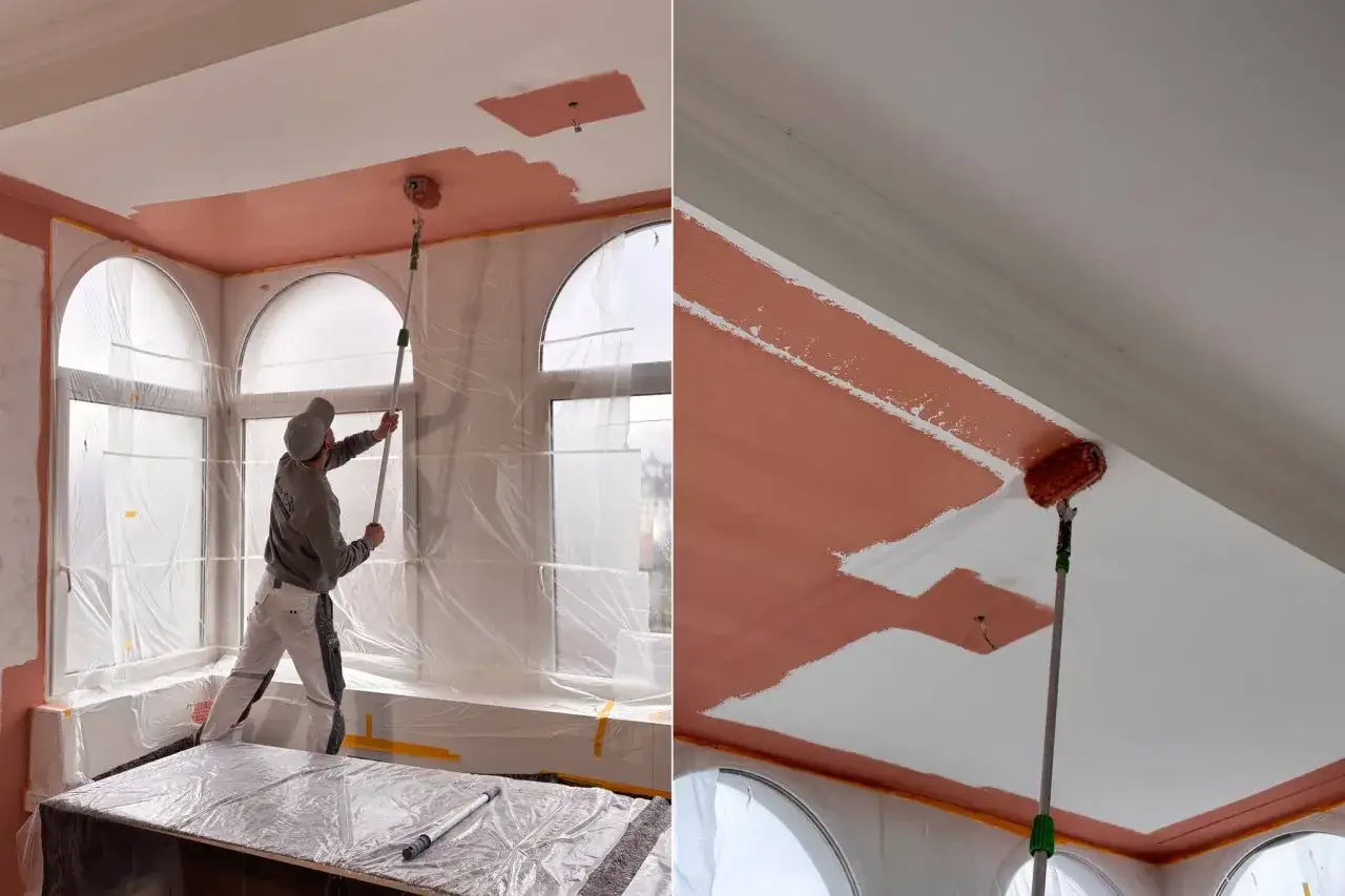 Maler streicht die Decke mit einer L-f&ouml;rmigen Rolle. Der Raum ist mit Folie abgedeckt, um ihn vor Farbspritzern zu sch&uuml;tzen.