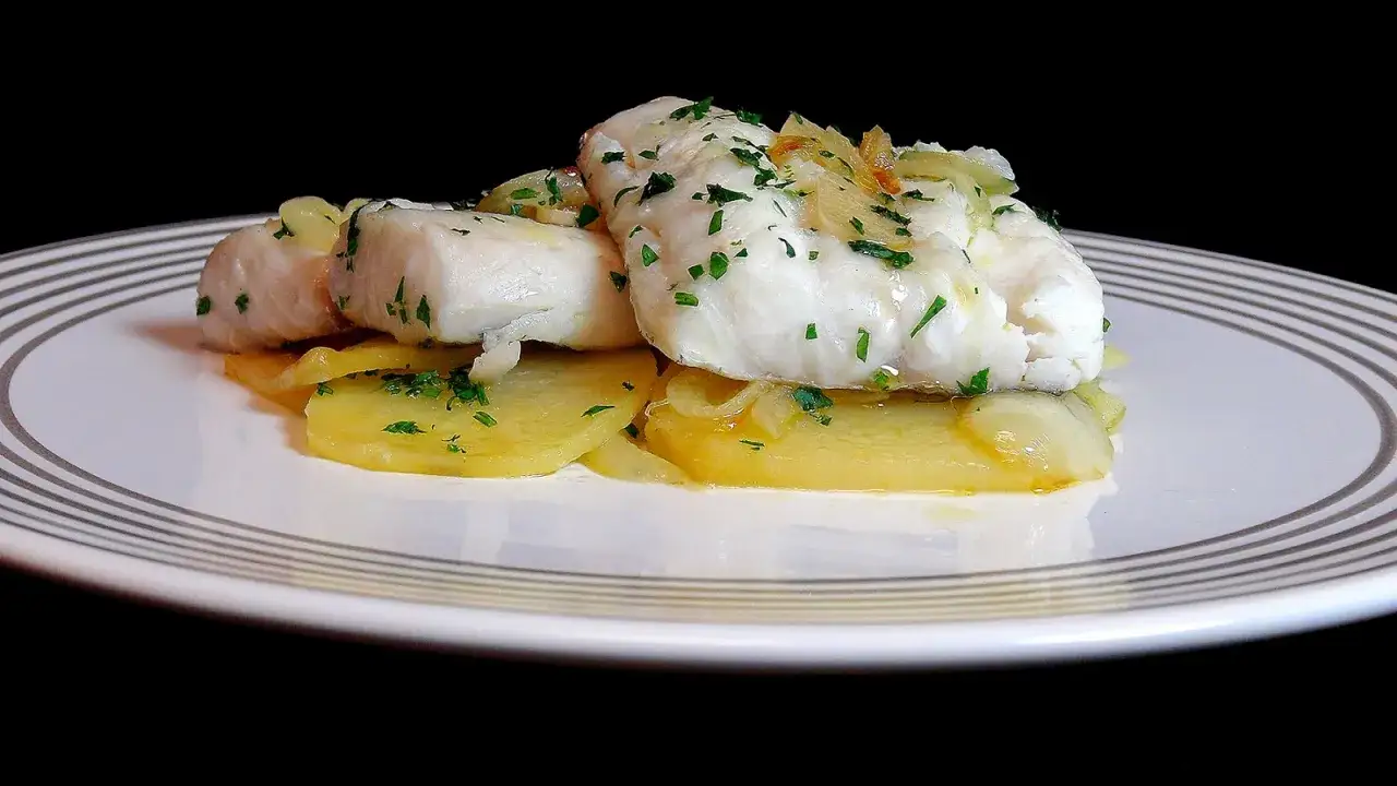 Cogote de merluza servido sobre patatas laminadas y espolvoreado con perejil picado.