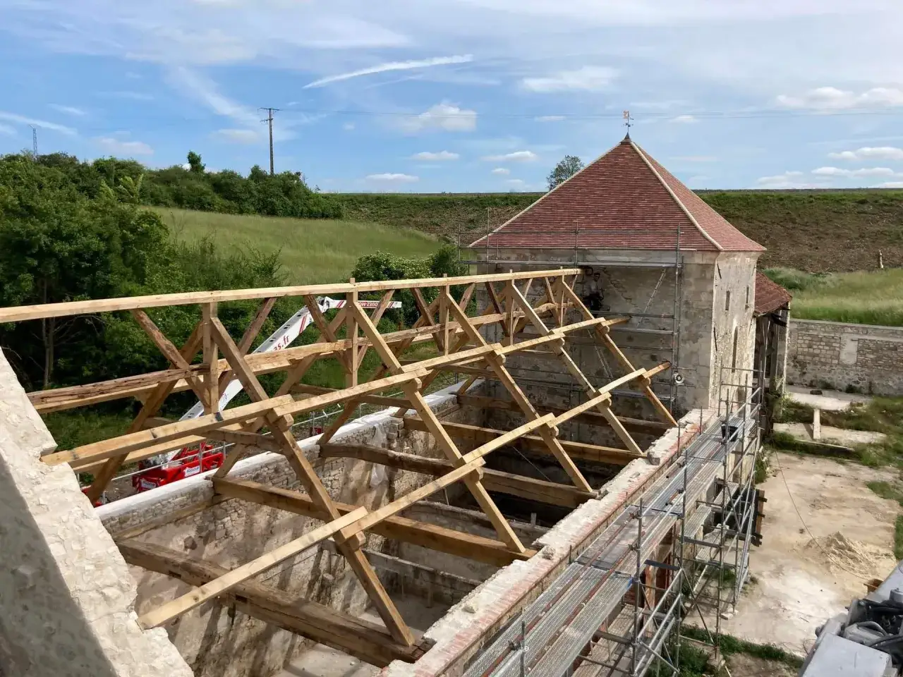 Un chantier de r&eacute;novation d'un vieux b&acirc;timent, avec une charpente en **vers blanc bois** en cours de construction, sous un ciel bleu.