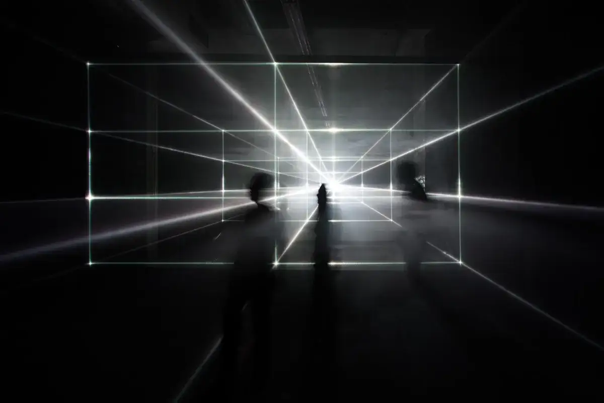 Abstract architectural photography captures blurred figures within a luminous grid of light beams, creating a sense of depth and mystery.