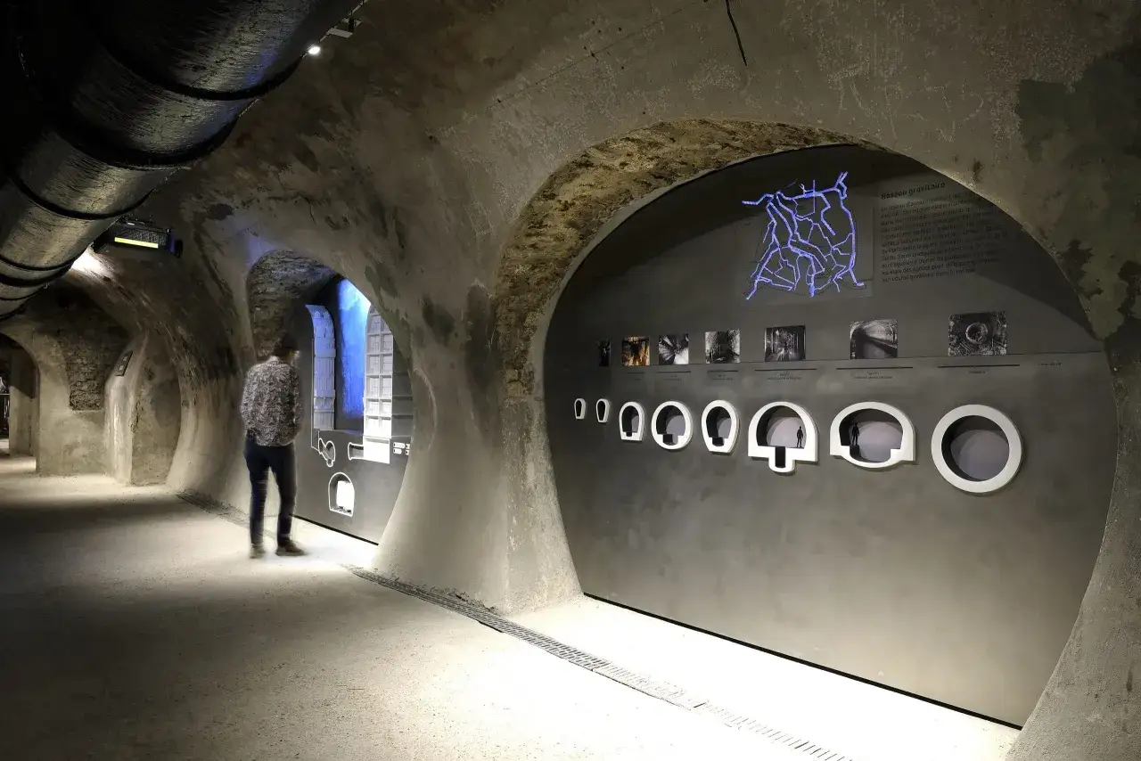 Visite du mus&eacute;e des &eacute;gouts de Paris. Un visiteur observe une exposition sur le r&eacute;seau d'assainissement dans un tunnel vo&ucirc;t&eacute;.