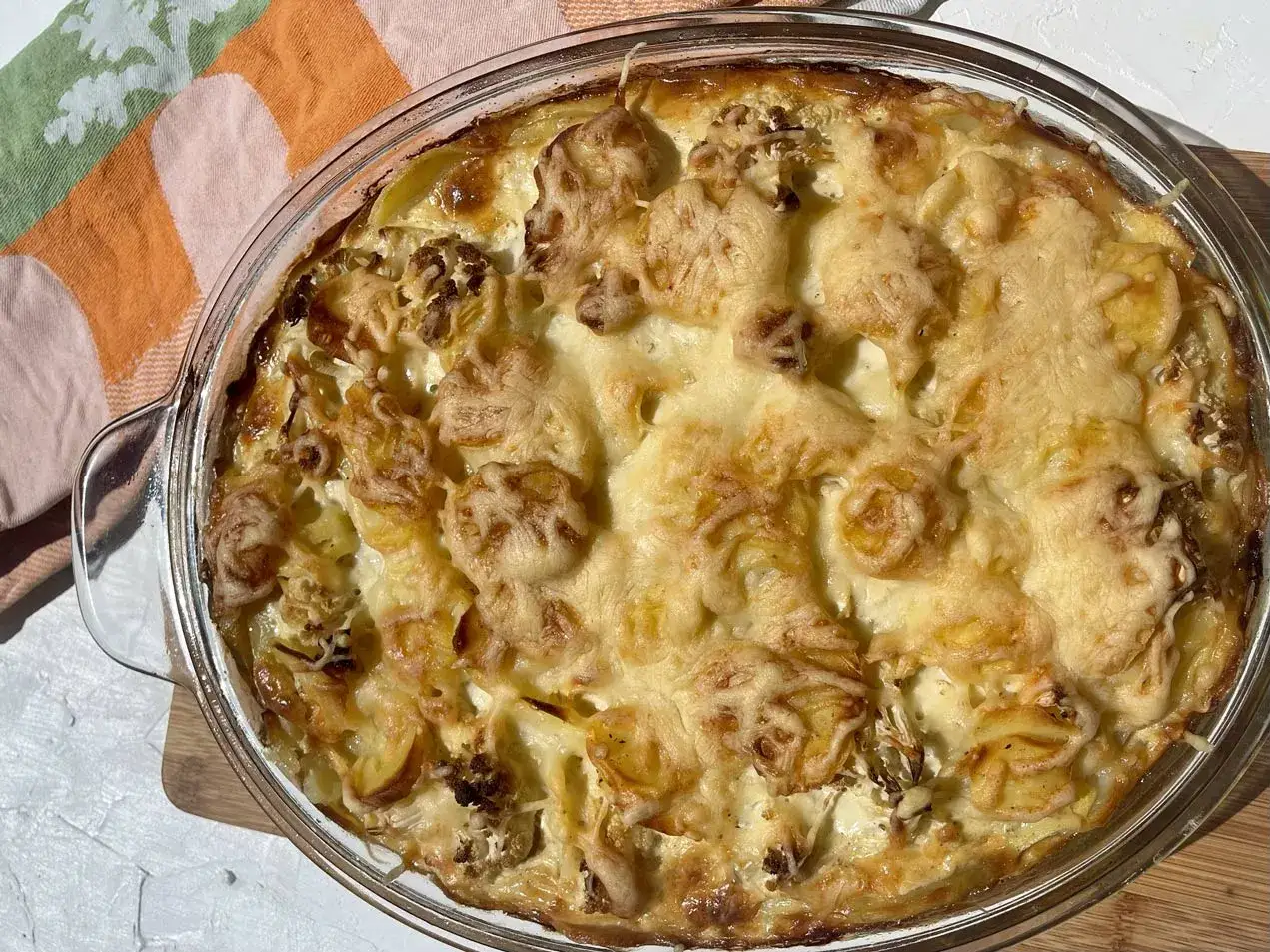 Ein goldbraun überbackener blumenkohl kartoffel auflauf in einer Glasform, mit geschmolzenem Käse bedeckt.