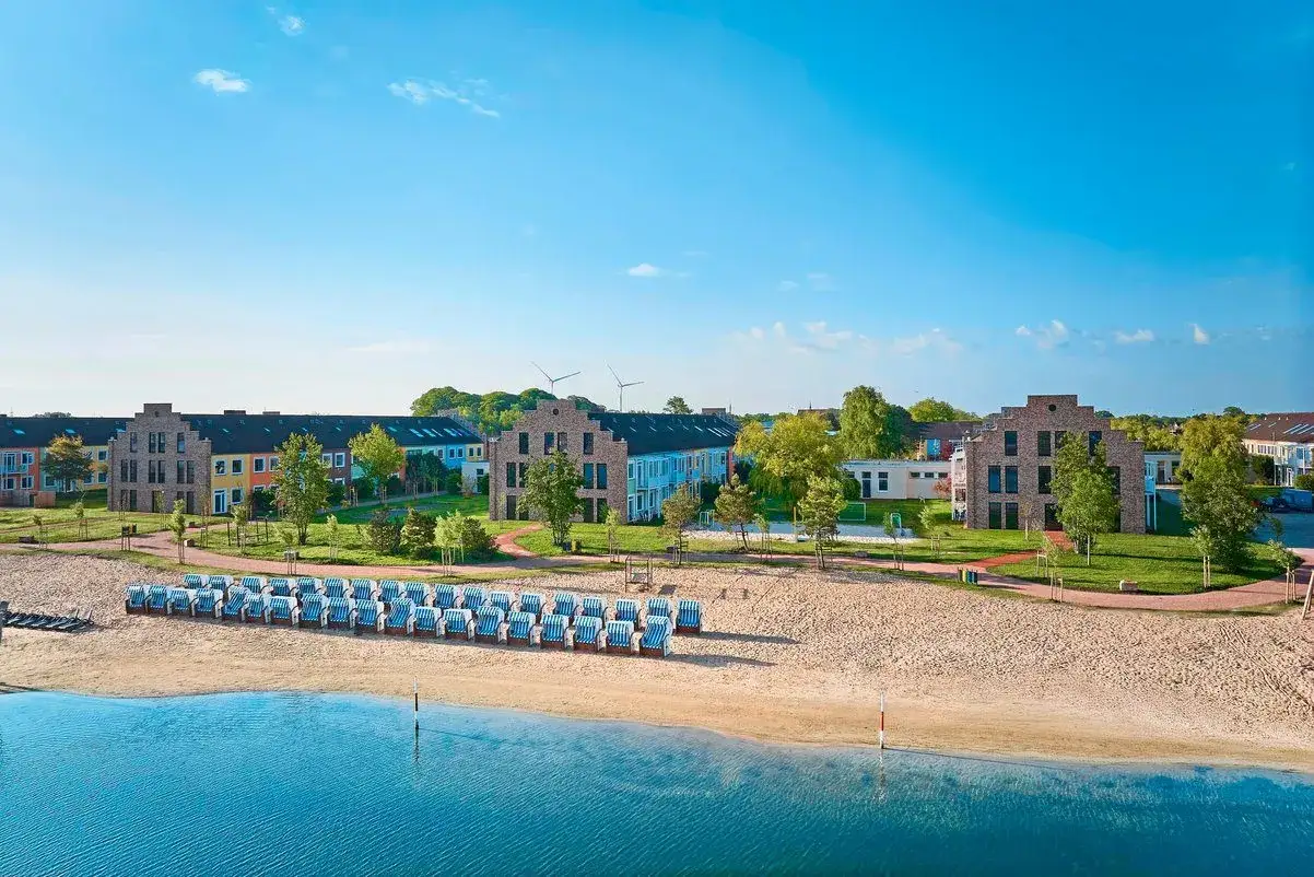 Blick auf das Wangerland Resort mit bunten Häusern, Strandkörben und blauem Wasser unter klarem Himmel.