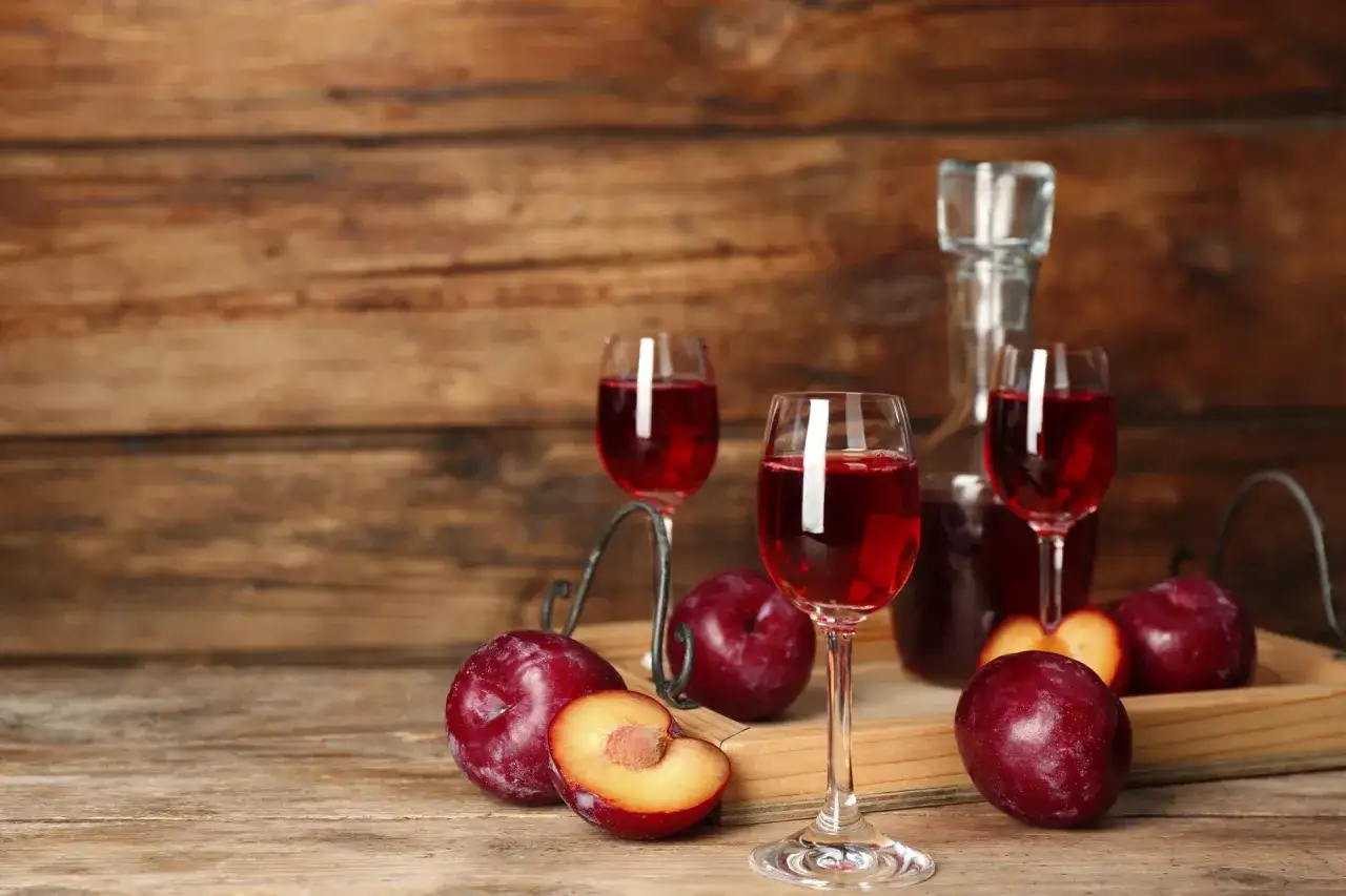 Rotwein mit wenig Tannin, serviert mit frischen Pflaumen auf einem Holztisch.
