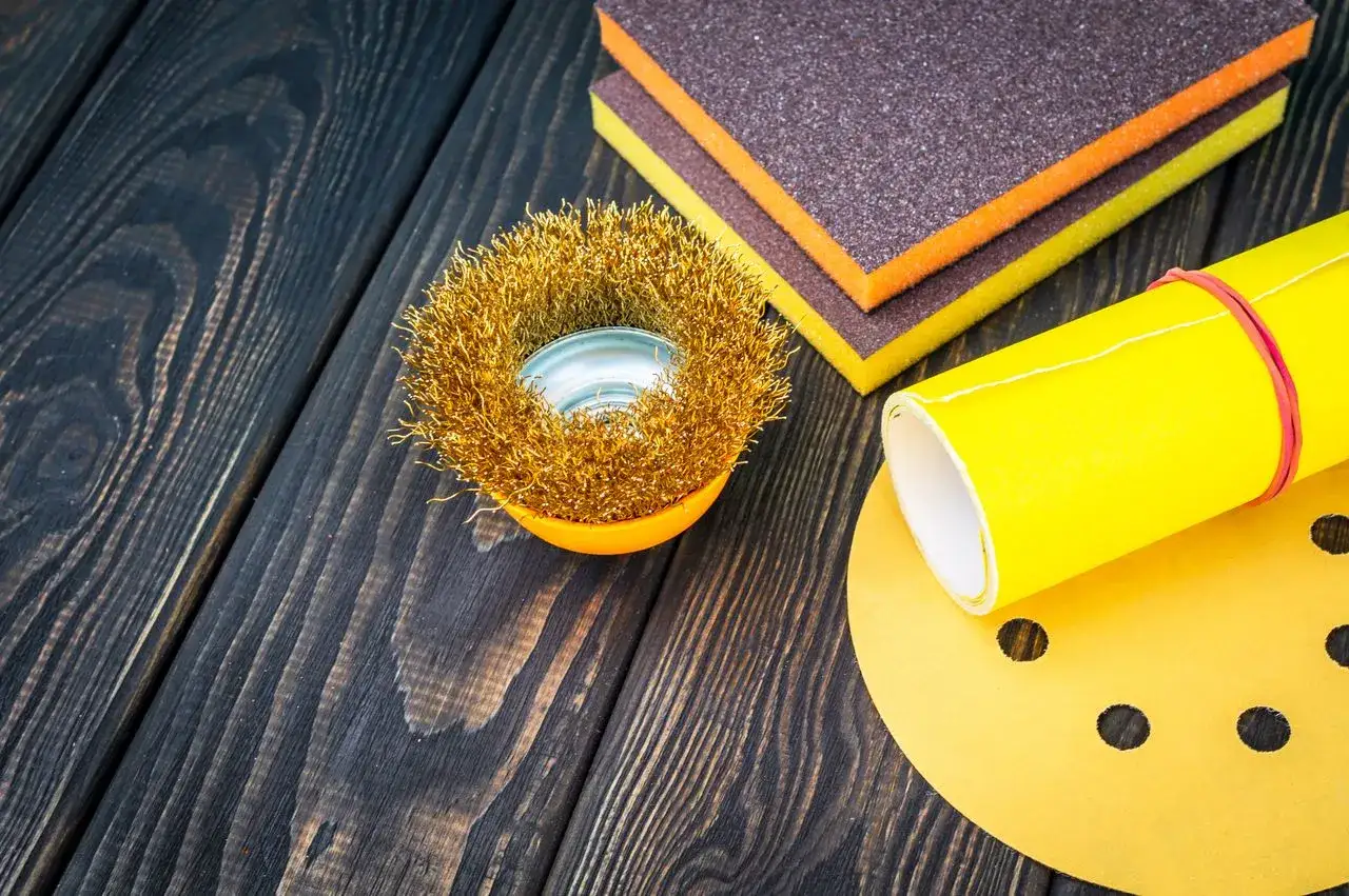 Préparation avant de savoir comment utiliser l'époxy : brosse métallique, éponges abrasives et papier de verre sur fond de bois sombre.