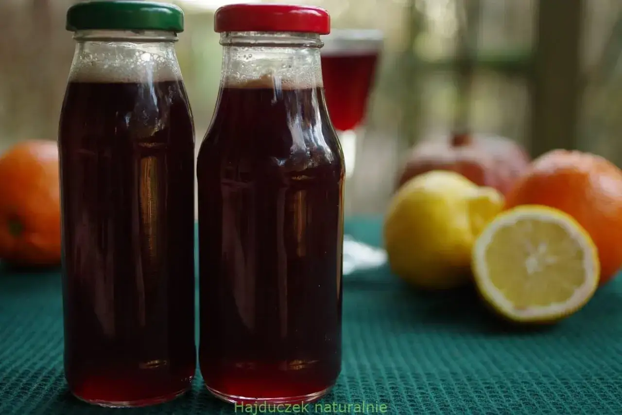 Dwa słoiki z ciemnym napojem, prawdopodobnie drink z grenadyną, obok pomarańczy i cytryn.