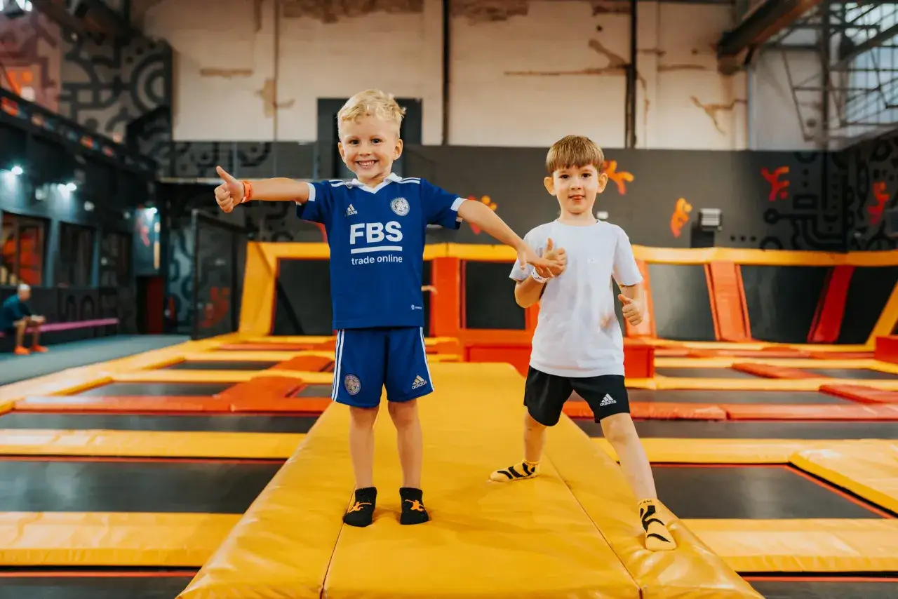 Dwóch chłopców na trampolinach w Warszawie świętuje Dzień Dziecka. Uśmiechnięci, pokazują kciuki w górę.