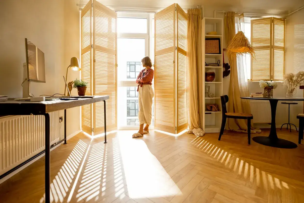 Una donna guarda fuori dalla finestra, mentre il sole crea ombre sul parquet che scricchiola.