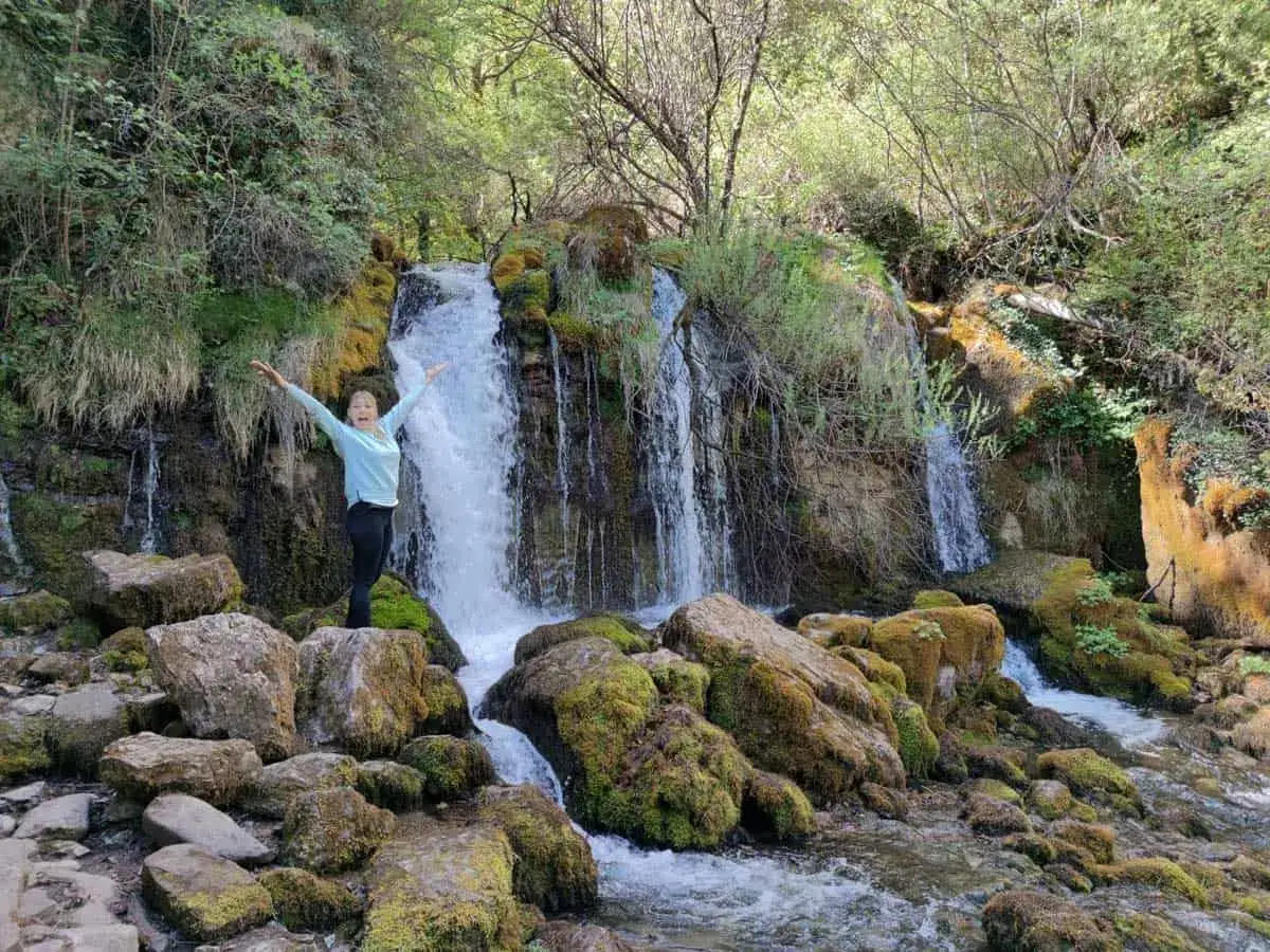 Una mujer celebra en la dou del Bastareny, rodeada de rocas cubiertas de musgo y la cascada en pleno esplendor.