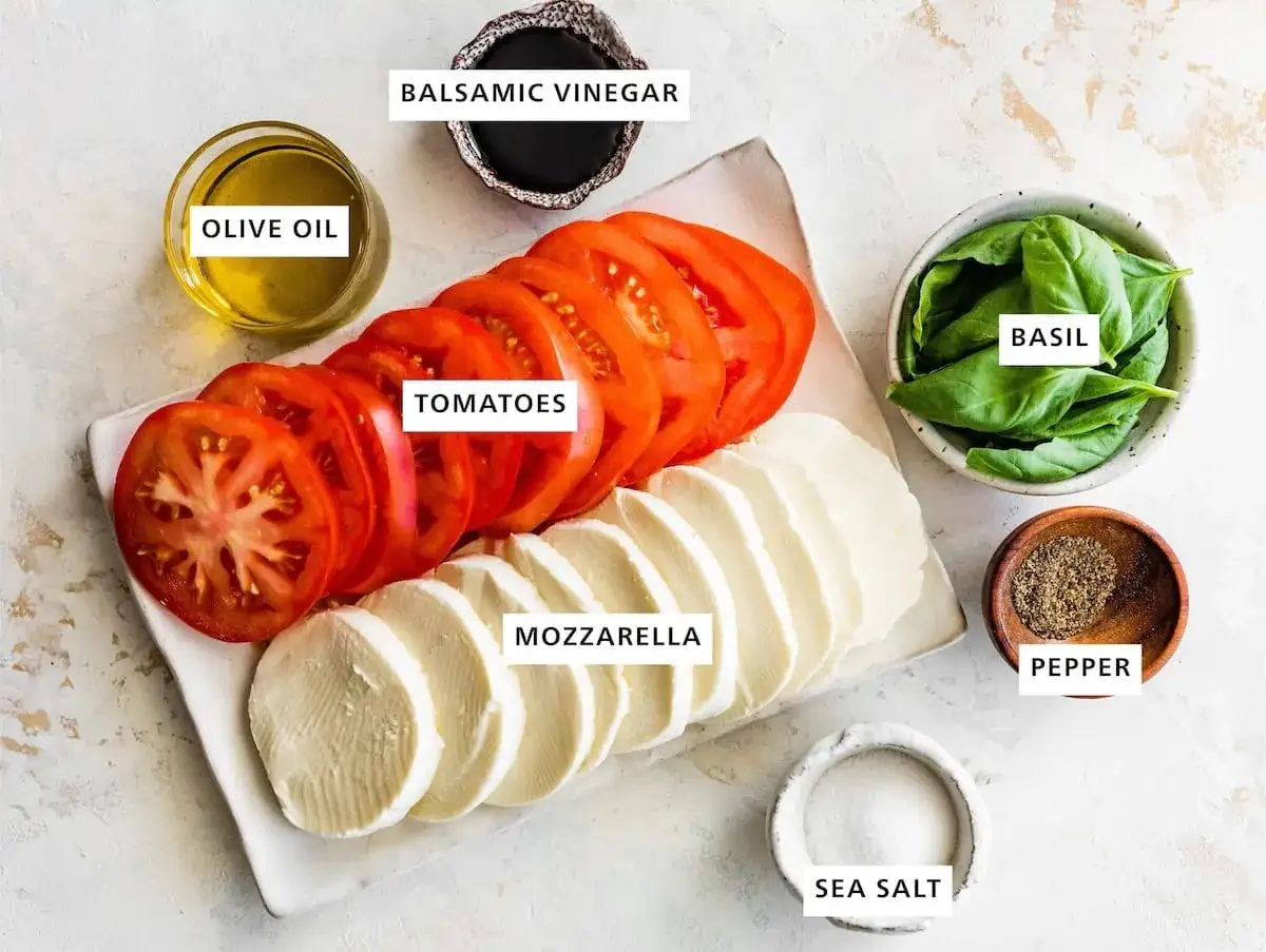 Zutaten für eine klassische Insalata Caprese: Tomatenscheiben, Mozzarella, Basilikum, Olivenöl, Balsamico, Salz und Pfeffer.
