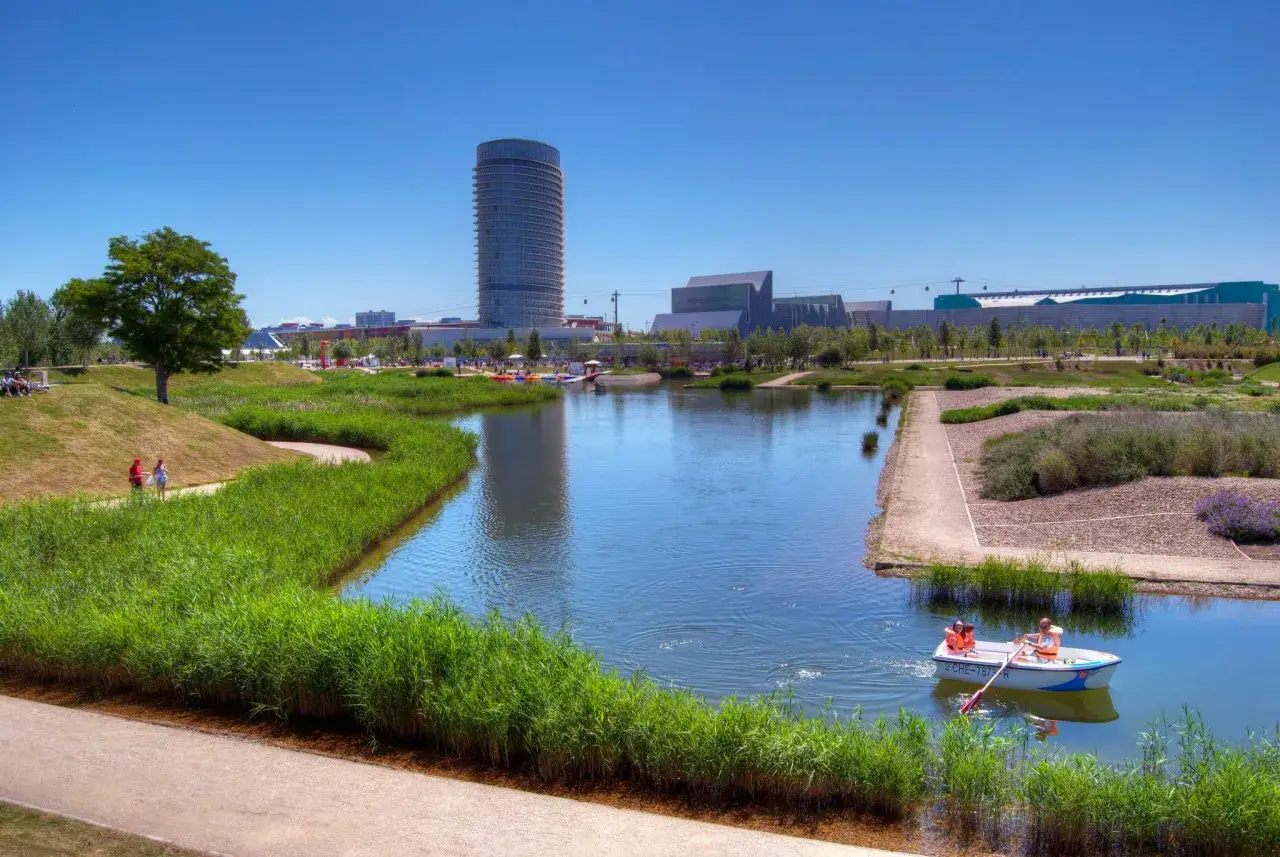Un paseo en barca por el lago del Anillo Verde de Zaragoza, con edificios modernos al fondo.