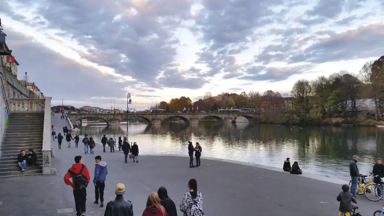 Passeggiata serale sui **murazzi Torino**, con gente che cammina e ammira il fiume e il ponte illuminato.