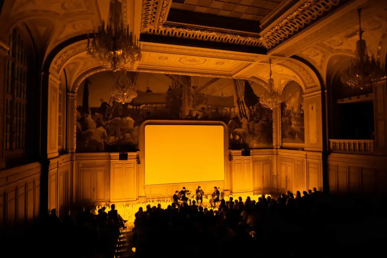 Concert intime &agrave; Paris, &eacute;clair&eacute; par la douce lueur de la **candlelight**. L'orchestre joue devant un &eacute;cran jaune, dans une salle orn&eacute;e de fresques et de lustres.