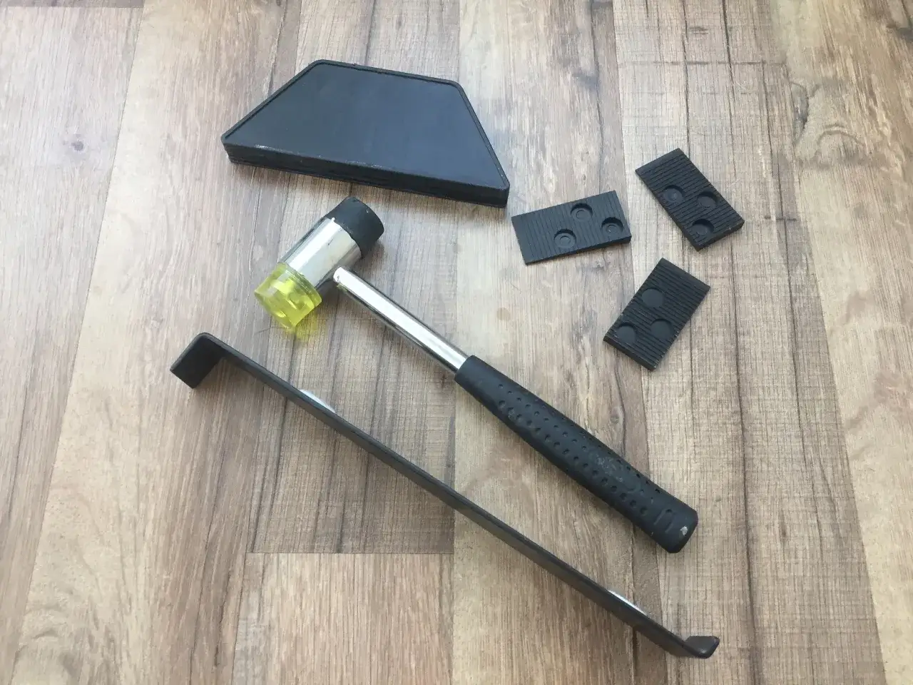 Tools for how to lay laminate flooring in a hallway: rubber mallet, pull bar, tapping block, and wedges.