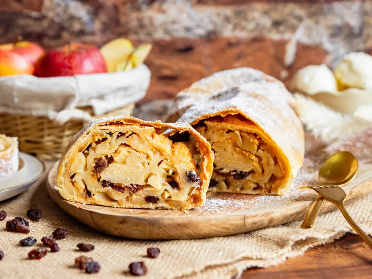 Apfelstrudel-Rezept von Landfrauen: goldbrauner Strudel mit Äpfeln und Rosinen, bestäubt mit Puderzucker. Dazu ein Löffel Eis.