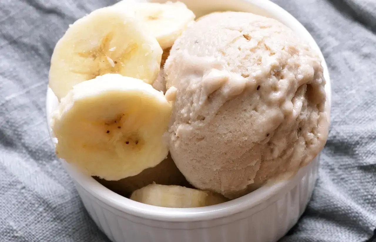 Delicioso helado de plátano cremoso servido en un cuenco blanco, adornado con rodajas frescas de plátano.