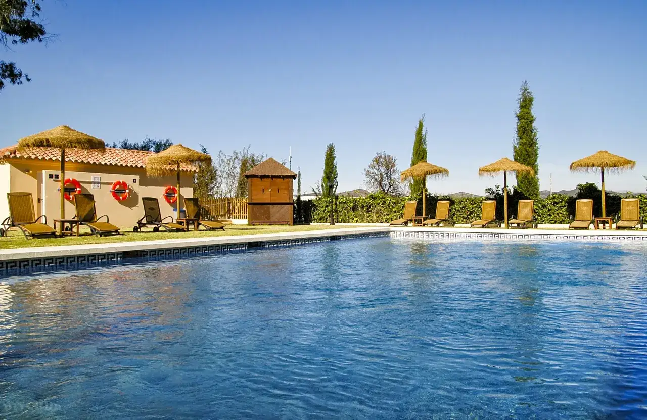 Piscina con tumbonas y sombrillas de paja, ideal para disfrutar de los mejores camping Andaluc&iacute;a.