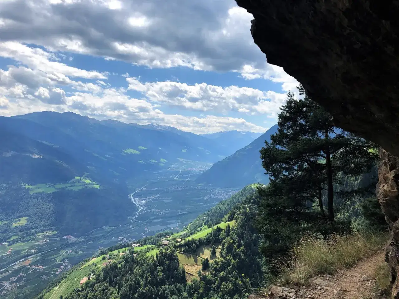 Blick aus einer Felsnische auf ein gr&uuml;nes Tal mit Bergkette. Ein Baum ragt ins Bild. Perfekt f&uuml;r hiking deutsch.