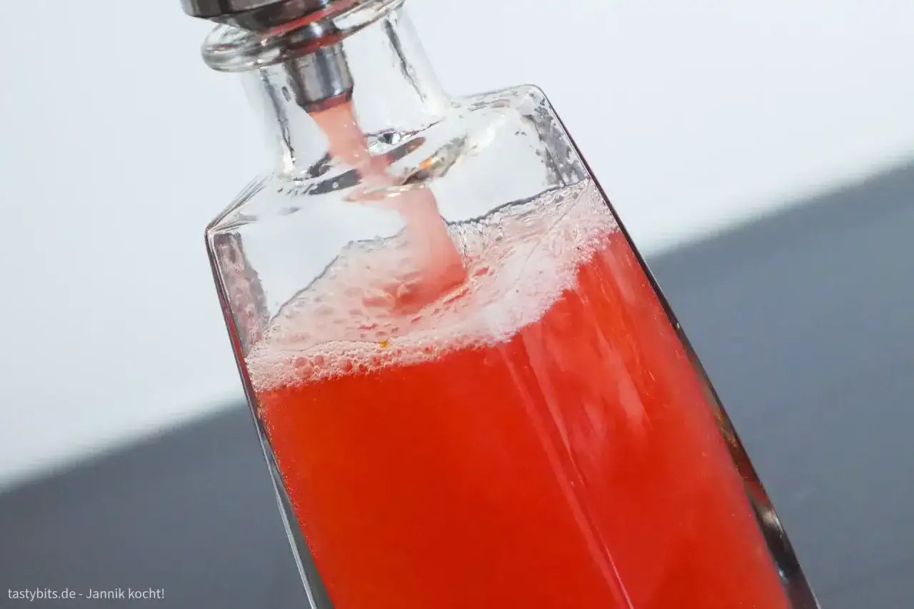 Frisch zubereiteter Rhabarbersirup fließt schäumend in eine Glasflasche. So einfach lässt sich Rhabarbersirup selber machen!