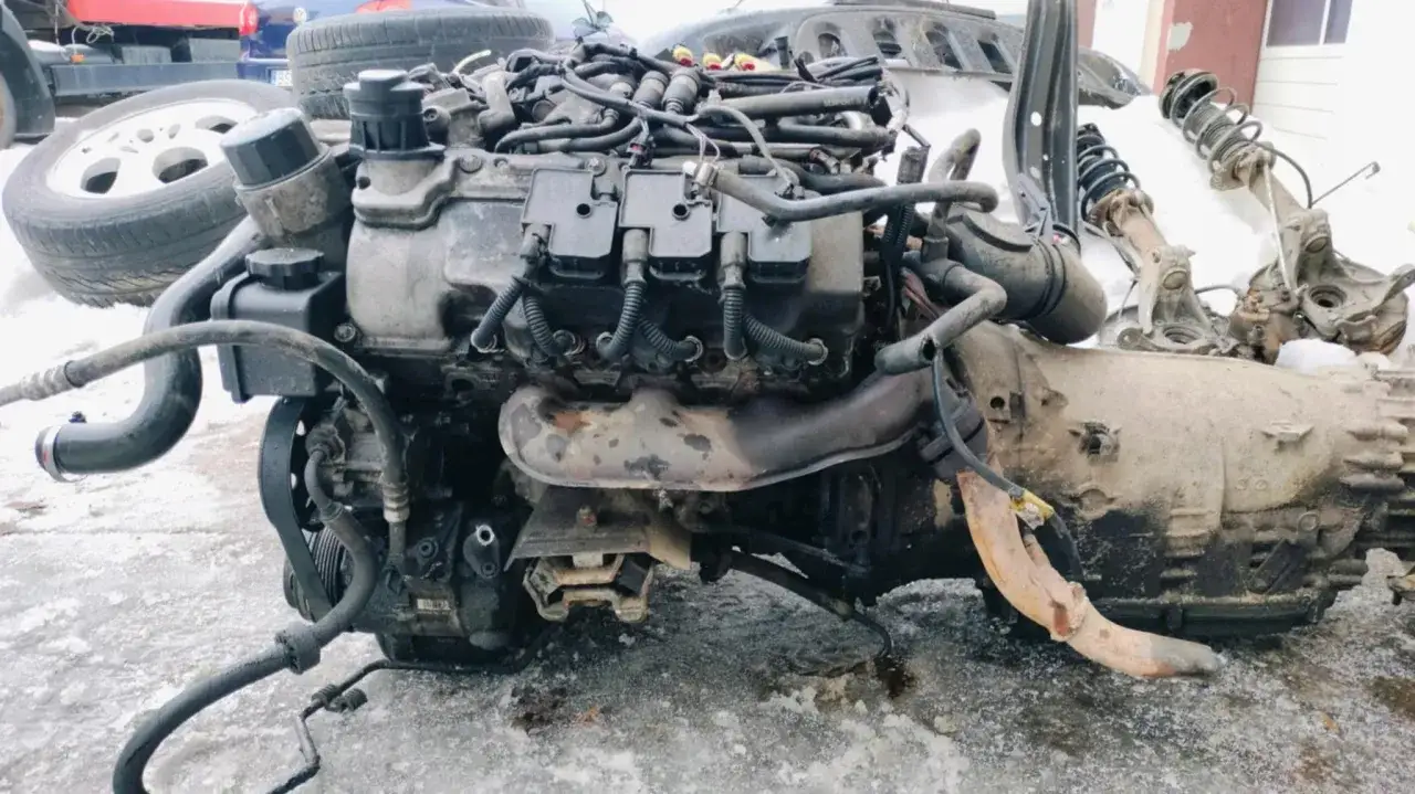 Silnik i skrzynia biegów z Mercedesa Benz ML, częściowo zdemontowane, leżą na śniegu.