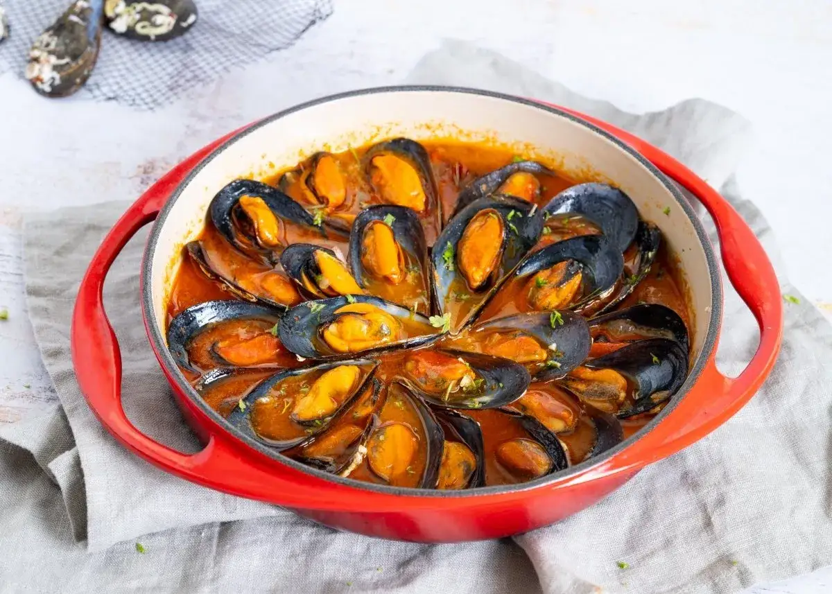 Mejillones en salsa roja, servidos en una cazuela roja, con perejil picado.