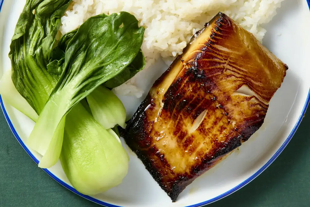 A perfectly grilled saikyo yaki fish fillet with a sweet glaze, served with fluffy white rice and vibrant green bok choy.