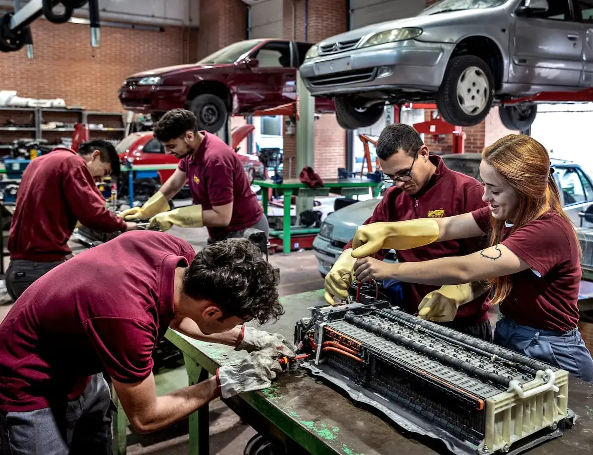 Estudiantes de grados medios en Barcelona trabajan en un taller mec&aacute;nico, reparando un componente de coche.