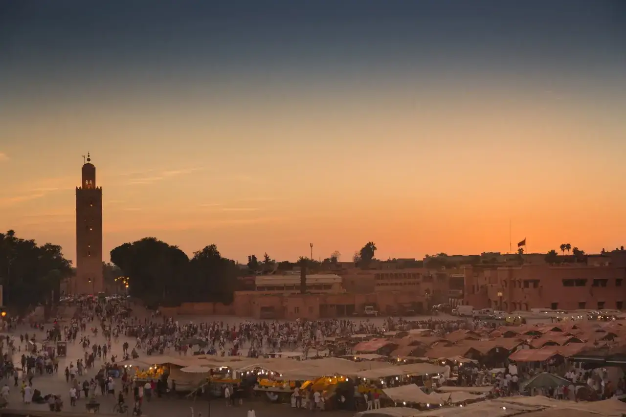Zachód słońca nad placem Dżamaa al-Fana w Marrakeszu. Tłumy ludzi, stragany i minaret Koutoubia tworzą niepowtarzalne marrakesz atrakcje.