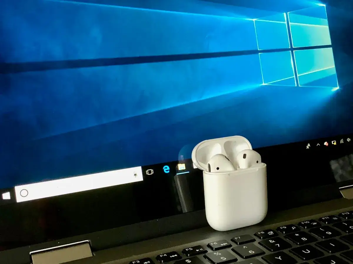 AirPods w etui na klawiaturze laptopa z systemem Windows. Dowiedz się, jak podłączyć AirPods do komputera Windows.