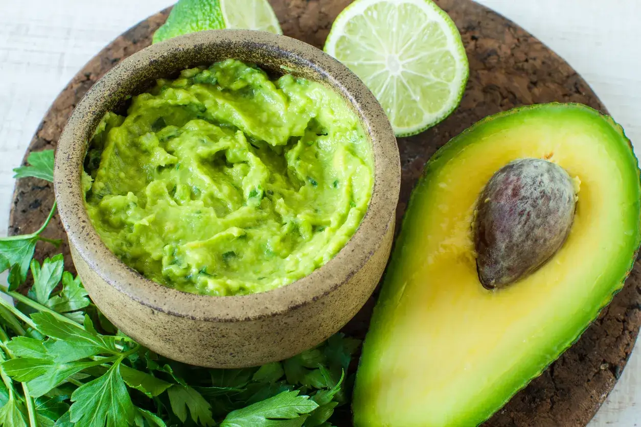Jak zrobić guacamole z awokado? Miseczka pysznego guacamole, poł&oacute;wka awokado, limonka i natka pietruszki.